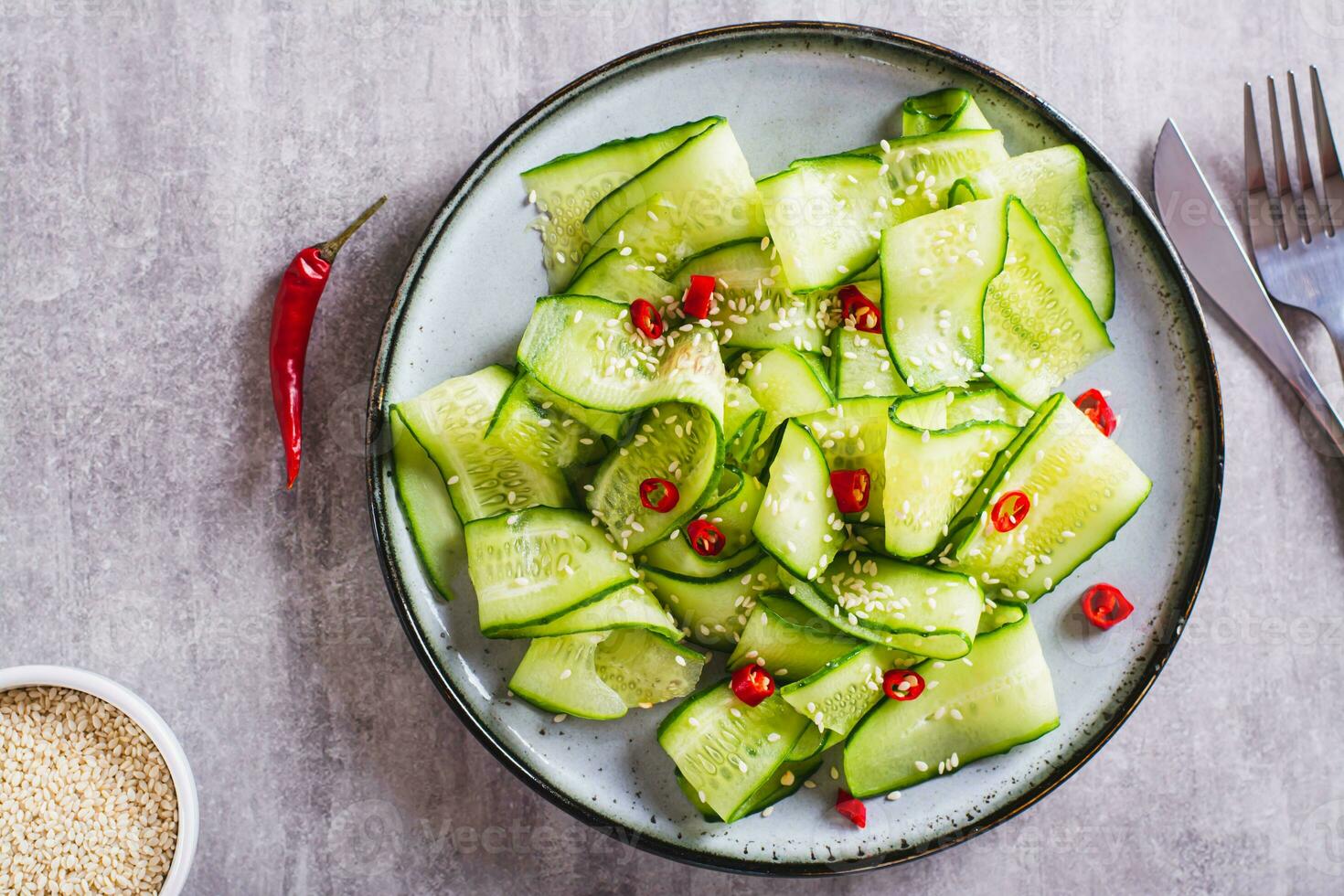 dichtbij omhoog van pittig salade van komkommer plakjes, heet rood peper en sesam zaden Aan een bord top visie foto