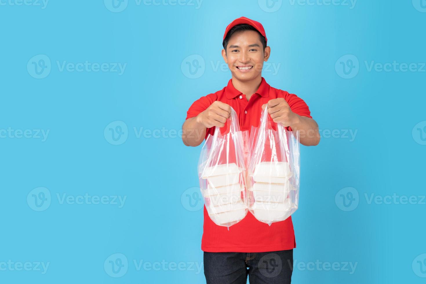 glimlachende bezorger werknemer in rode pet leeg shirt uniform staan met het geven van eten bestellen foto