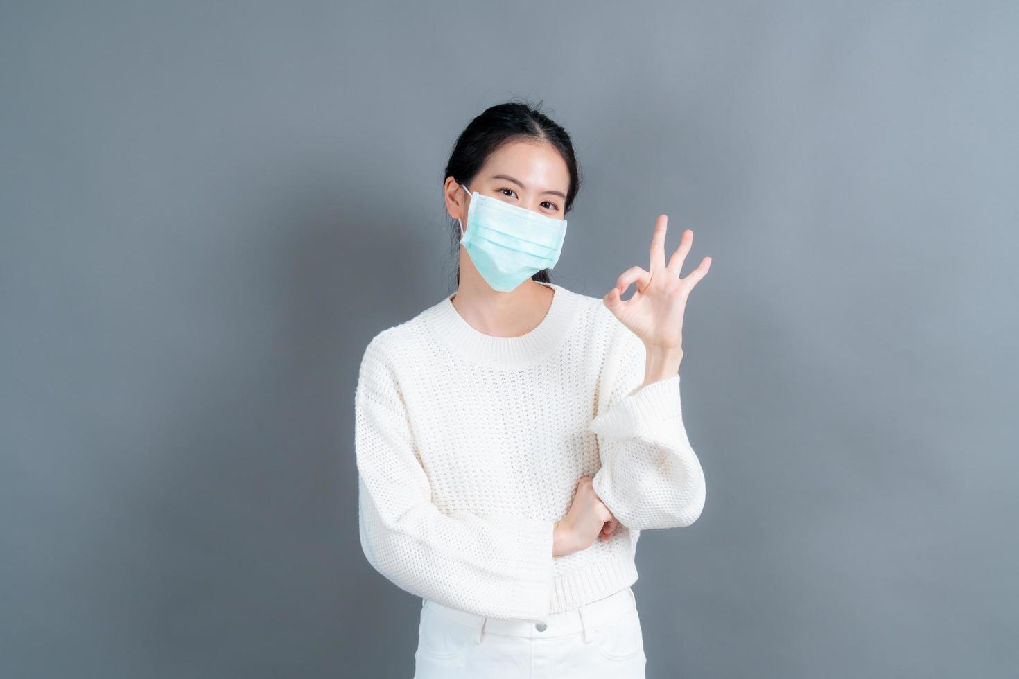 jonge aziatische vrouw die medisch gezichtsmasker draagt en ok teken toont foto