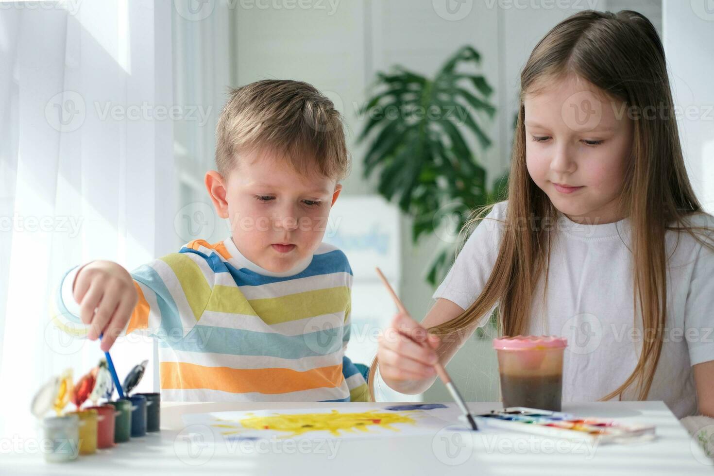 broer en zus trek een afbeelding met verven Aan een stuk van papier. kinderen zijn aan het leren naar tekenen. huis creativiteit. foto