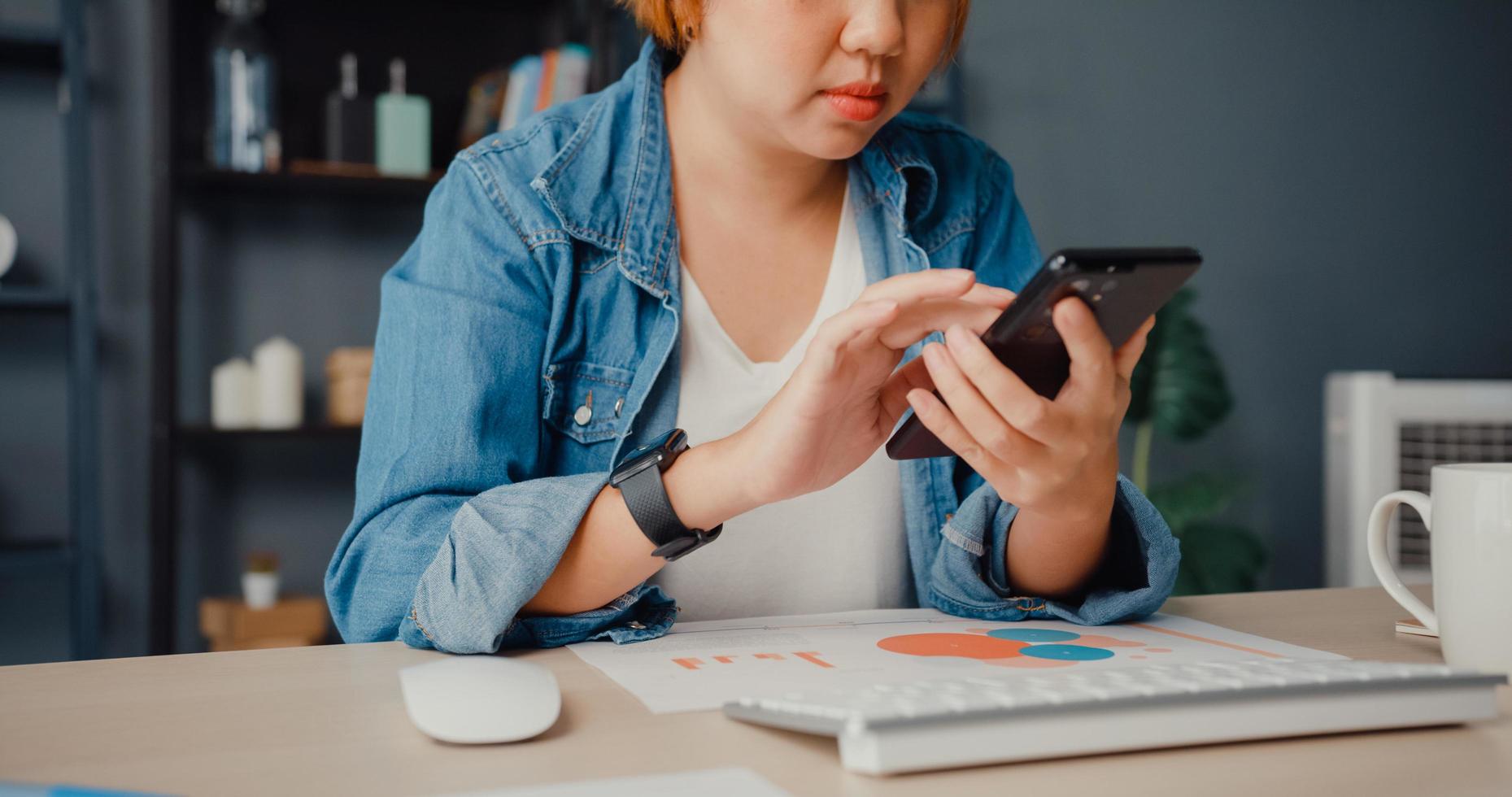 freelancer azië dame vrijetijdskleding met behulp van smartphone online winkelen via website zittend aan een bureau in de woonkamer foto