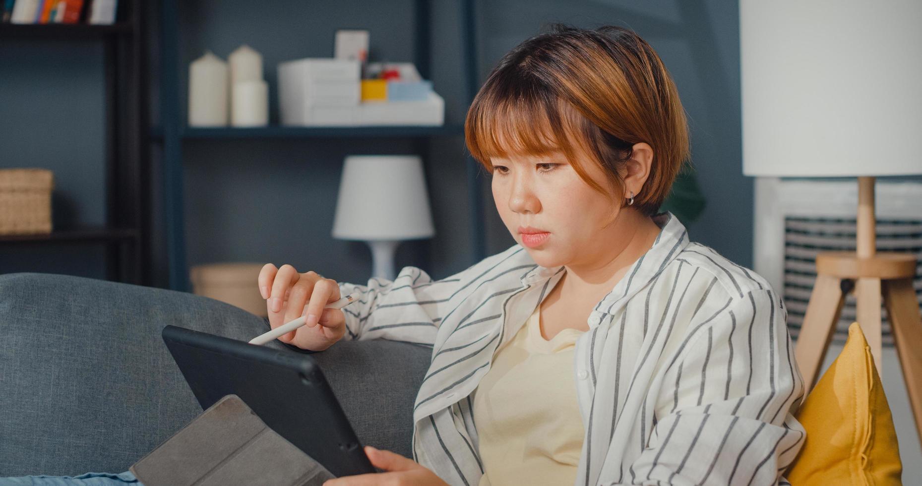 freelance aziatische dame vrijetijdskleding met behulp van tablet online leren in de woonkamer thuis foto