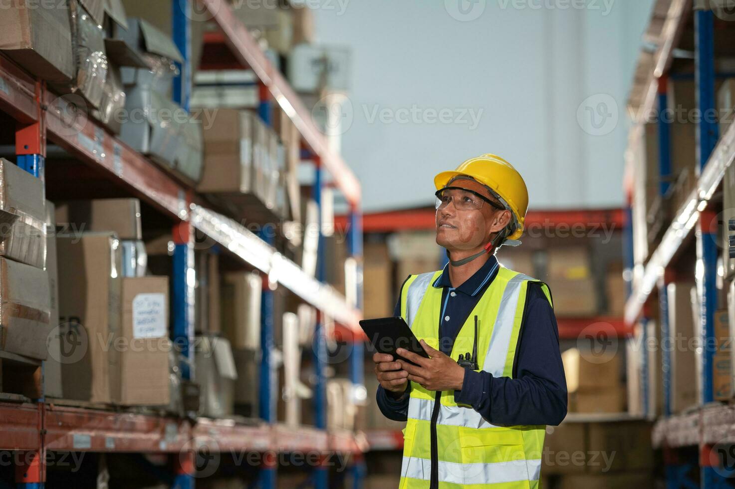 Aziatisch magazijn fabriek mannetje manager gelukkig gebruik makend van digitaal tablet communicatie gereedschap in een magazijn terwijl staand Aan een plank op zoek Bij de camera foto