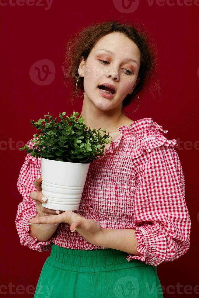 mooi vrouw stand-in en Holding bloem in pot rood achtergrond ongewijzigd foto