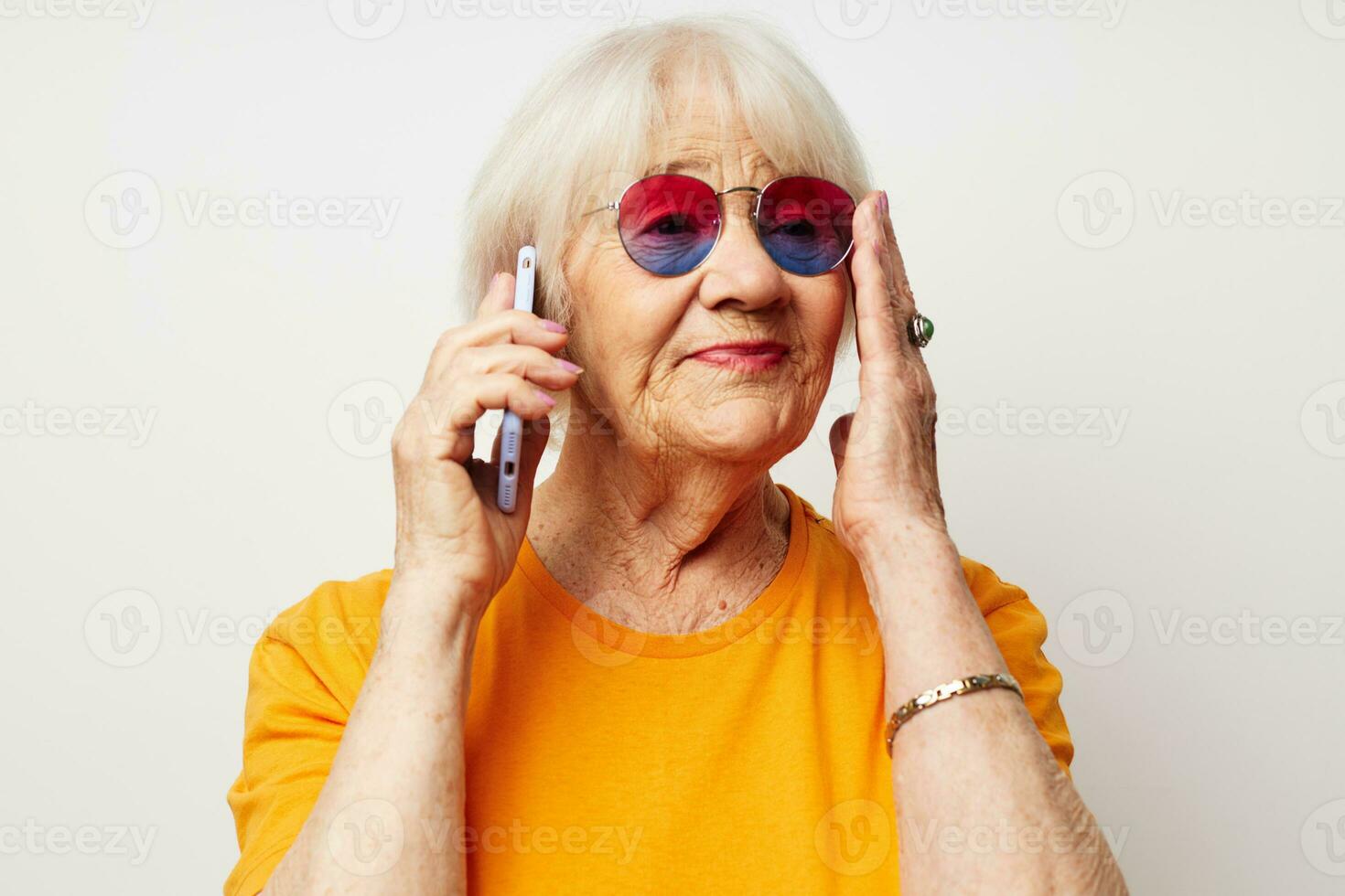 ouderen vrouw in gewoontjes t-shirt zonnebril pratend Aan de telefoon geïsoleerd achtergrond foto