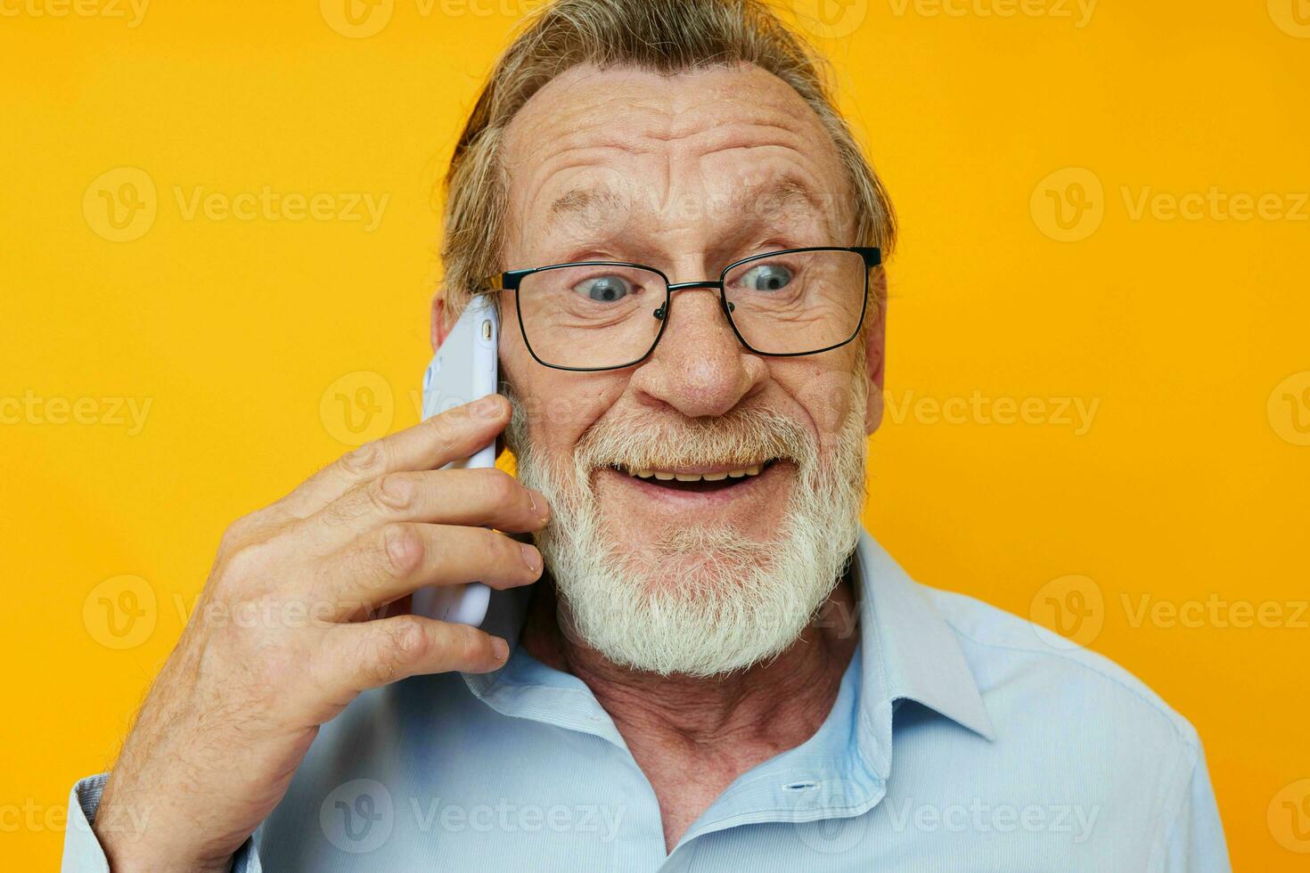 oud Mens in een blauw overhemd en bril pratend Aan de telefoon geel achtergrond foto