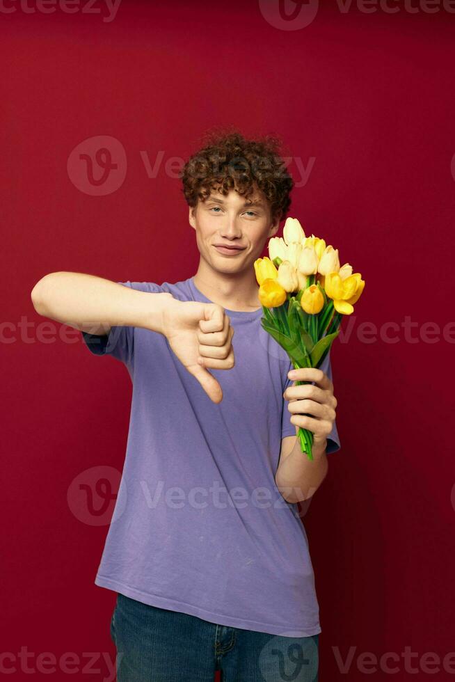 een jong Mens Holding een geel boeket van bloemen Purper t-shirts rood achtergrond ongewijzigd foto