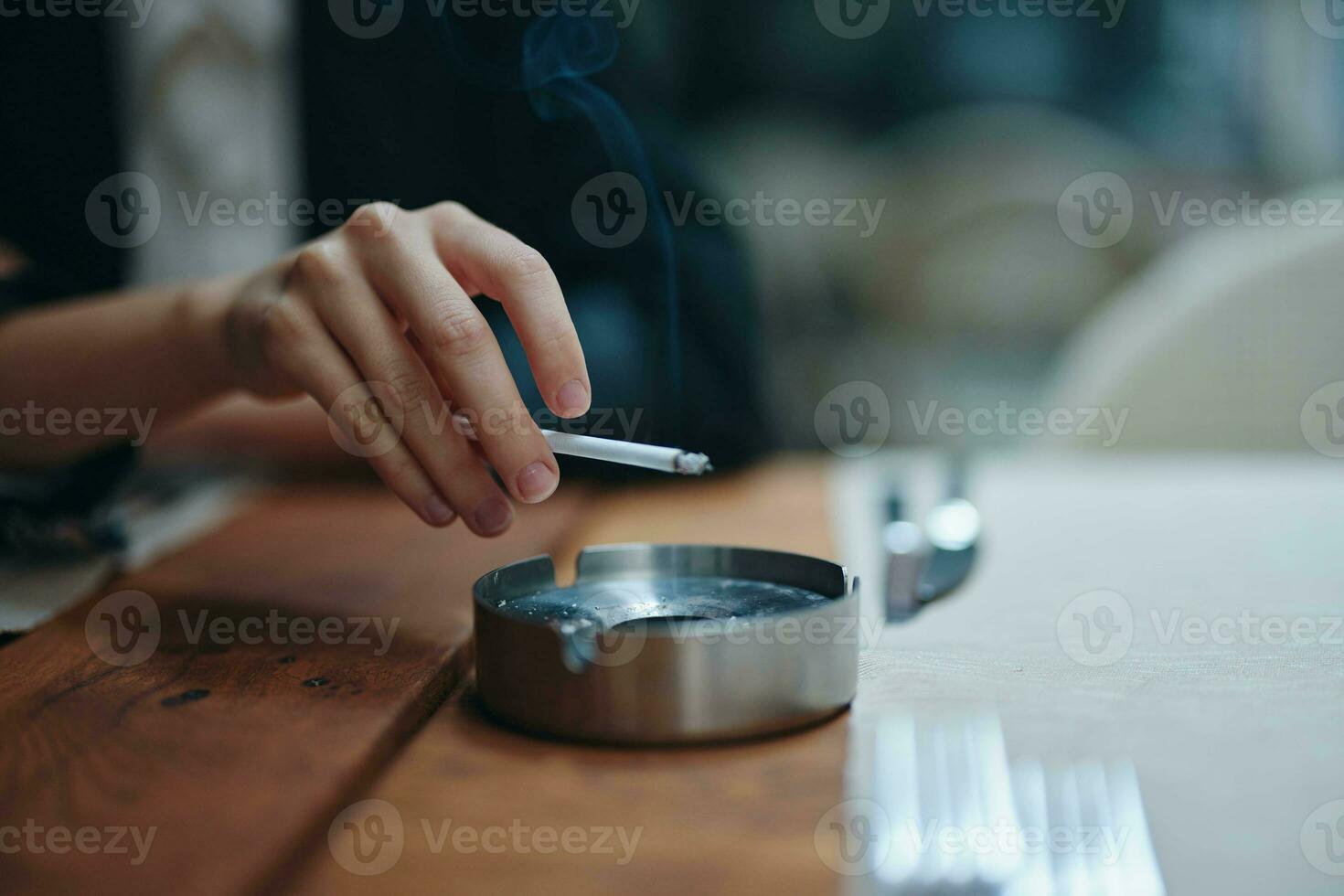 een vrouw met een sigaret in haar handen schudt de as in een asbakje, detailopname foto