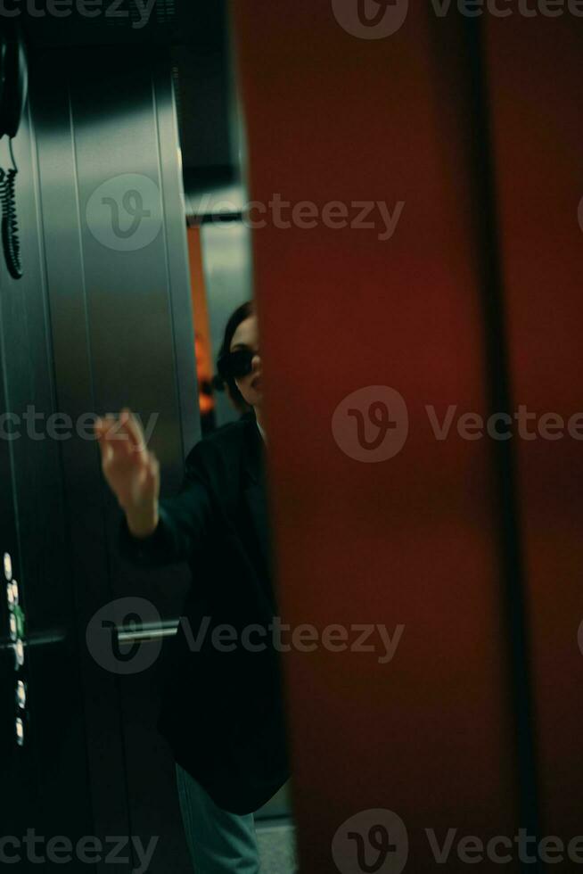 elegant vrouw in zwart jasje en zonnebril poseren in lift, mode model, donker filmische licht en kleur, aantrekkingskracht wijnoogst foto