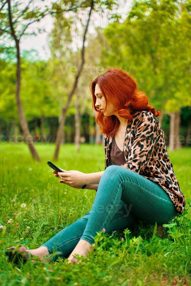 roodharige vrouw sms't terwijl ze op het gras zit foto