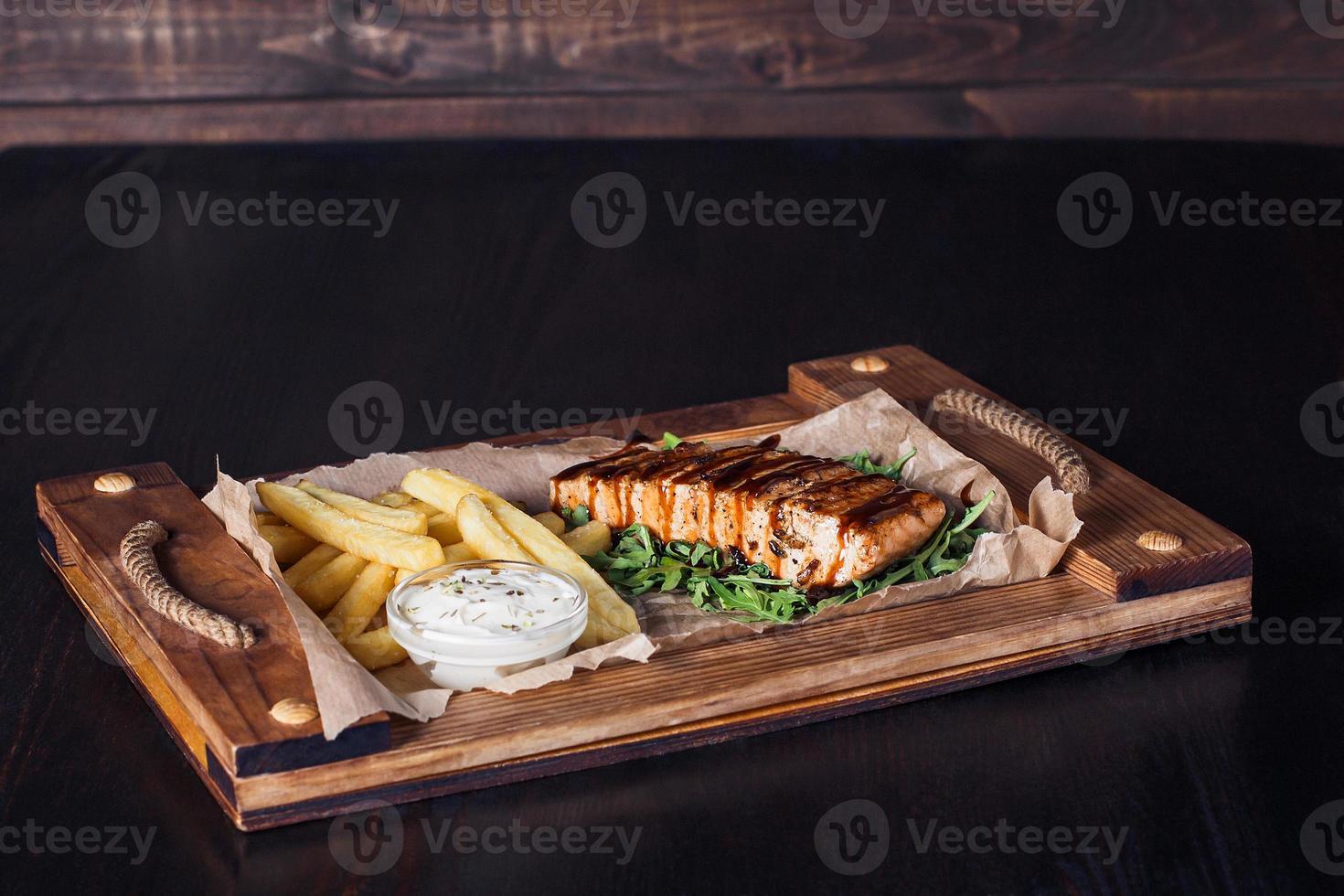 zalmfilet steak met frietjes op een houten dienblad, mooie portie, donkere achtergrond foto