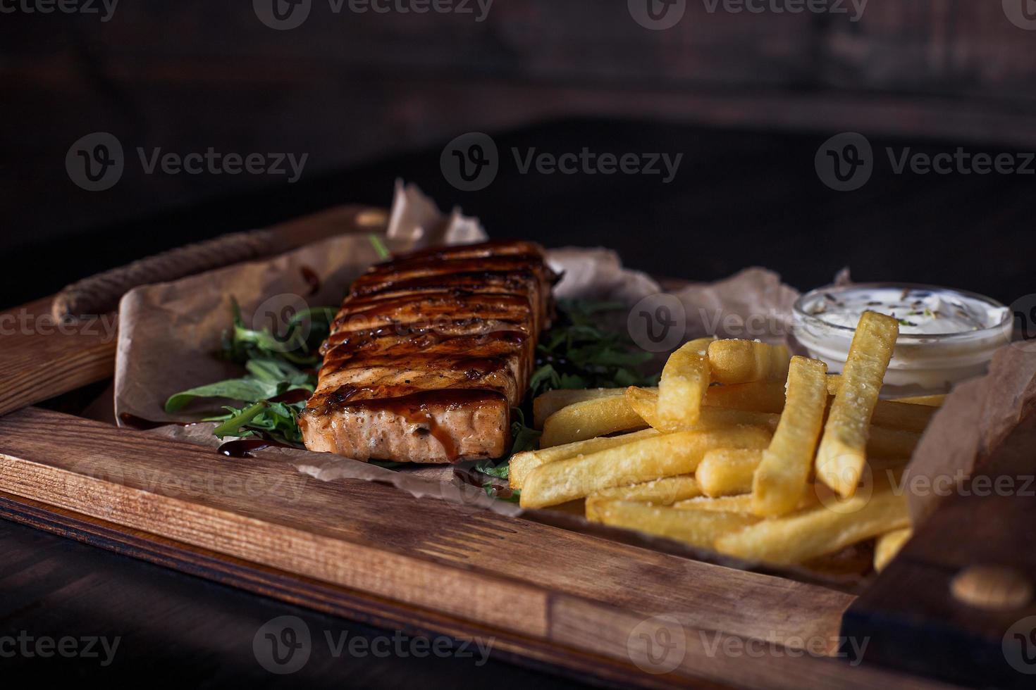 zalmfilet steak met frietjes op een houten dienblad, mooie portie, donkere achtergrond foto