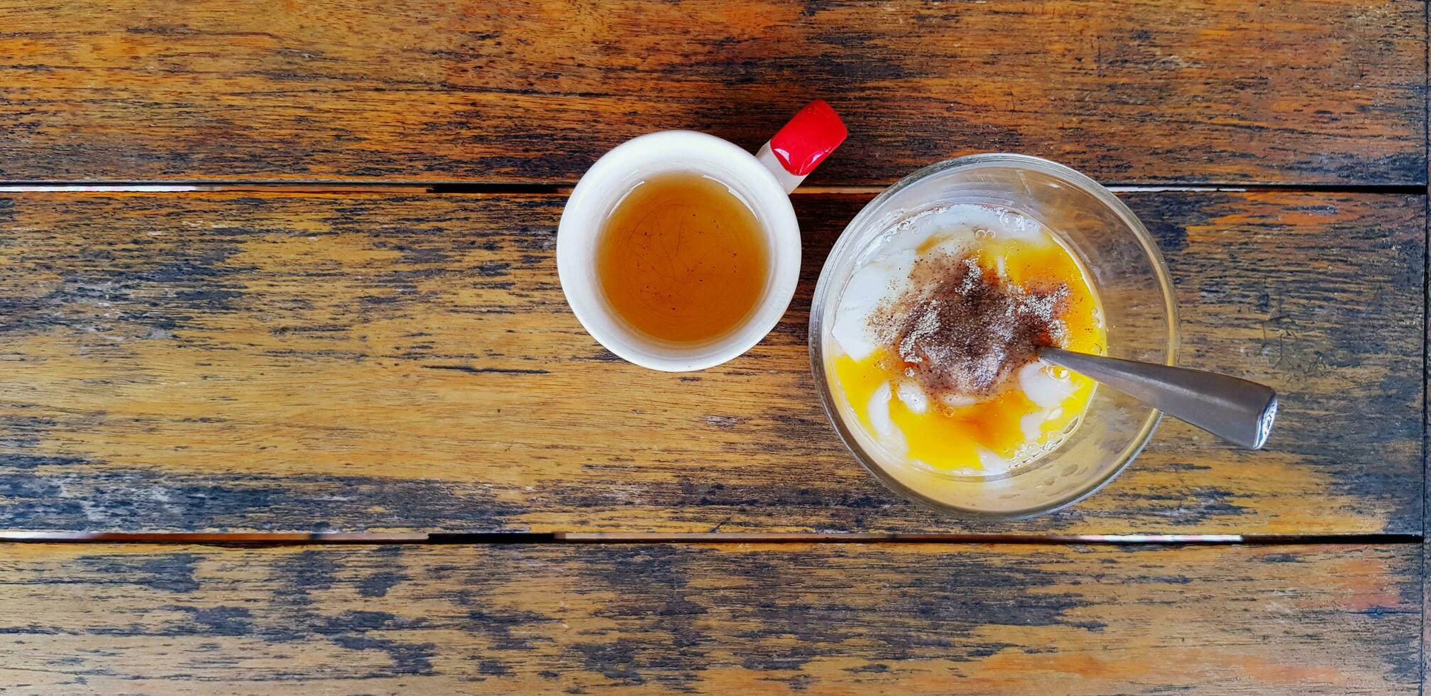 top visie van zacht gekookt eieren met thee lepel en klein kop van heet thee Aan bruin houten achtergrond of tafel met kopiëren ruimte. gezond voedsel en verfrissing drinken. foto