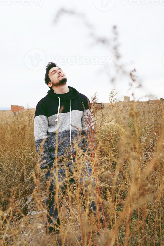 een jonge, aantrekkelijke man in rust met de ogen dicht en het hoofd omhoog in een geel buitenveld op een bewolkte dag foto