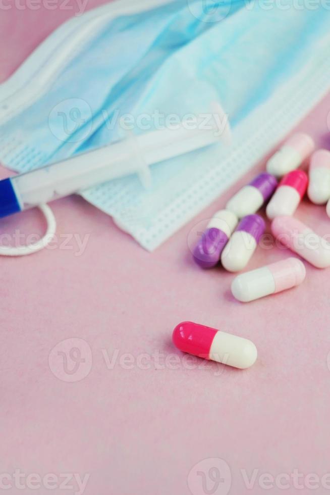 een gedetailleerde macro van een spuit door pillen op een medisch masker met roze achtergrond foto