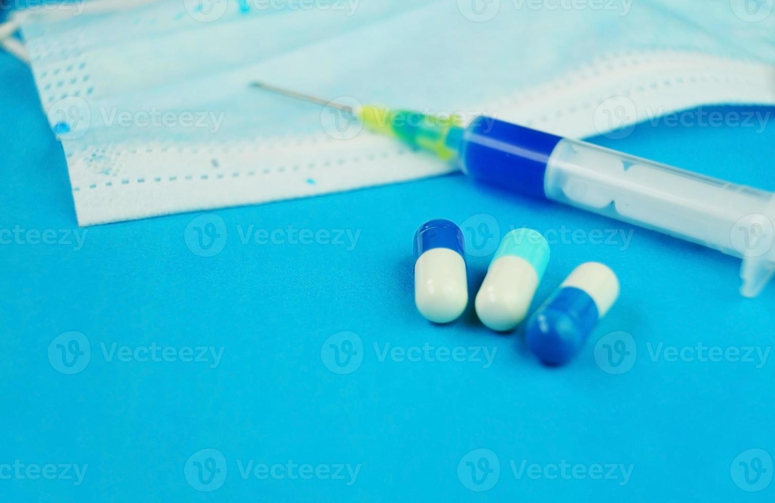 een gedetailleerde macro van een spuit door pillen met naald op een medisch masker met blauwe achtergrond foto