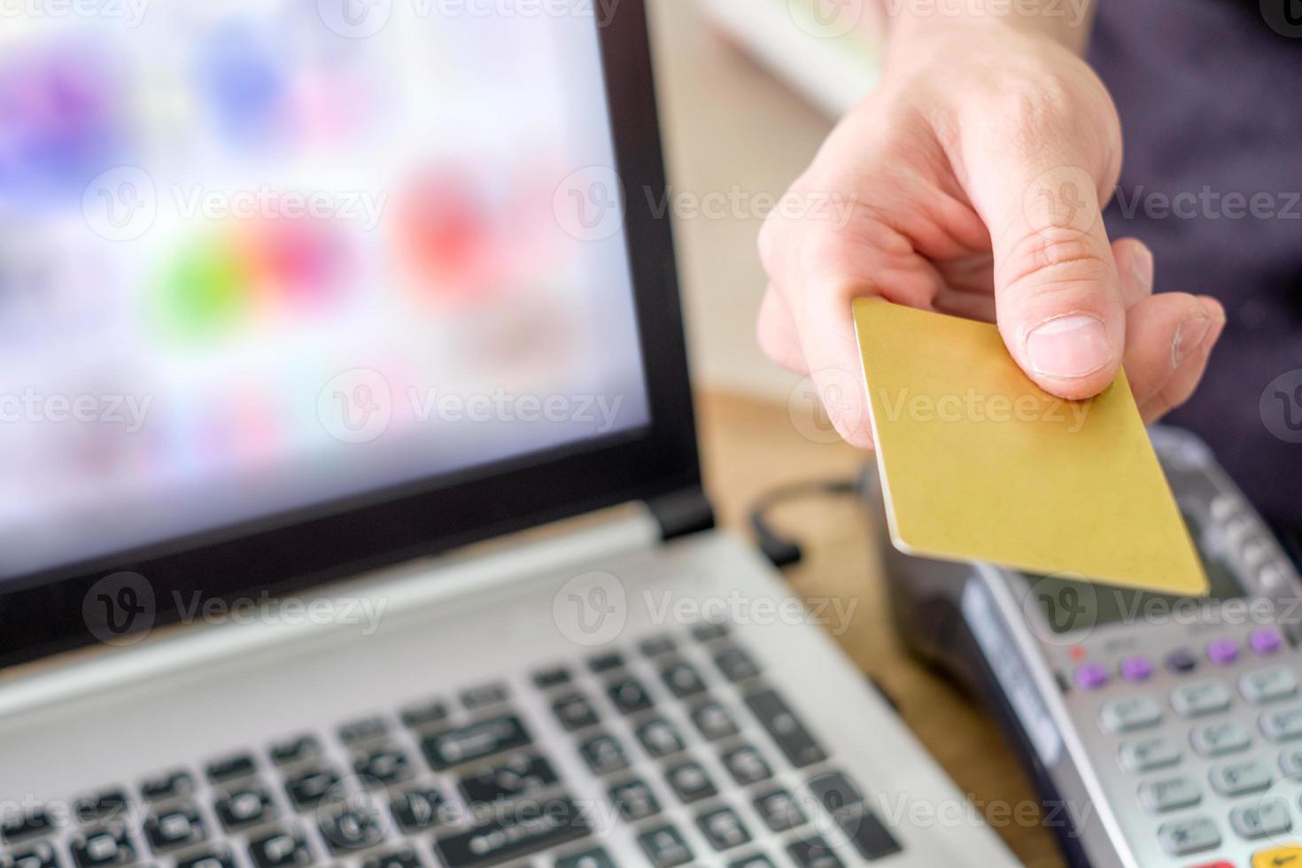 met de hand betalende creditcard op betaalterminal met laptop in de winkel foto