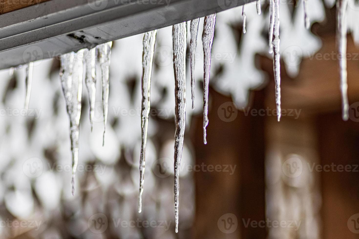 een grote transparante ijspegel hangt aan het dak van het huis. wintervorst foto