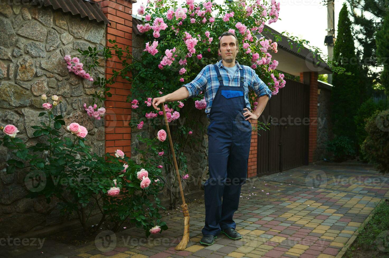 knap spaans tuinman met een bezem glimlacht Bij camera. mensen. professioneel. herenhuis schoonmaak en onderhoud concept foto