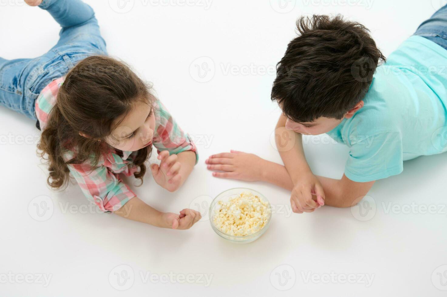top visie preteen jongen en schattig baby meisje, broer en zus aan het eten popcorn, aan het liegen Aan wit geïsoleerd studio achtergrond. foto