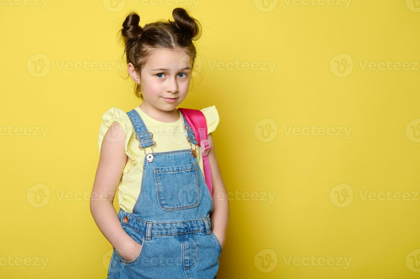 Kaukasisch lief kind meisje 6 jaren oud, draag- rugzak, Holding haar handen in zakken, vol vertrouwen op zoek Bij camera. foto