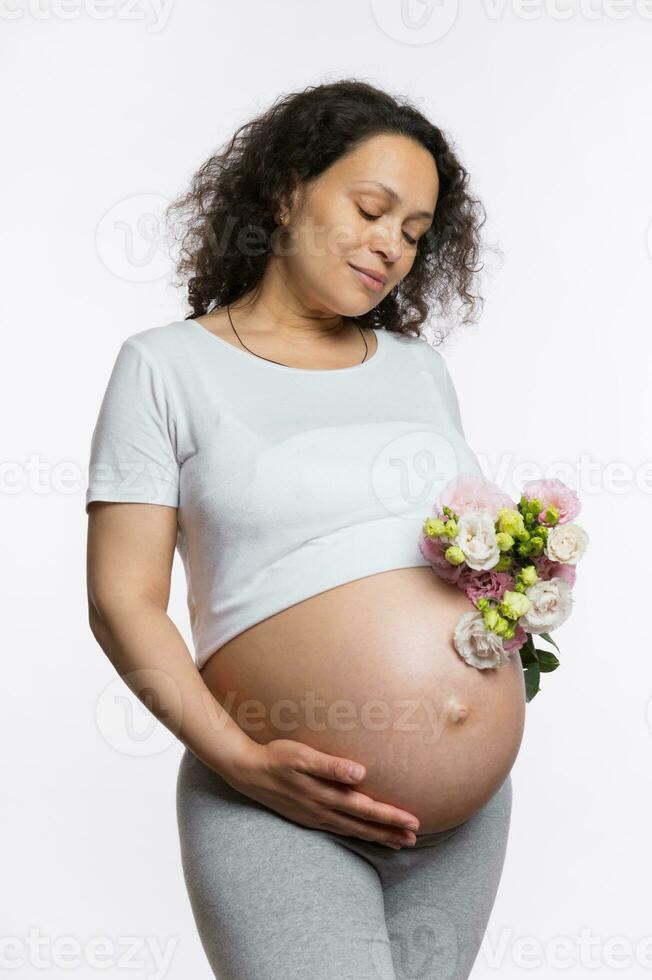 zwangerschap. moederschap. moeder dag concept. charmant zwanger vrouw met bundel van bloemen, Holding hand- Aan naakt buik foto