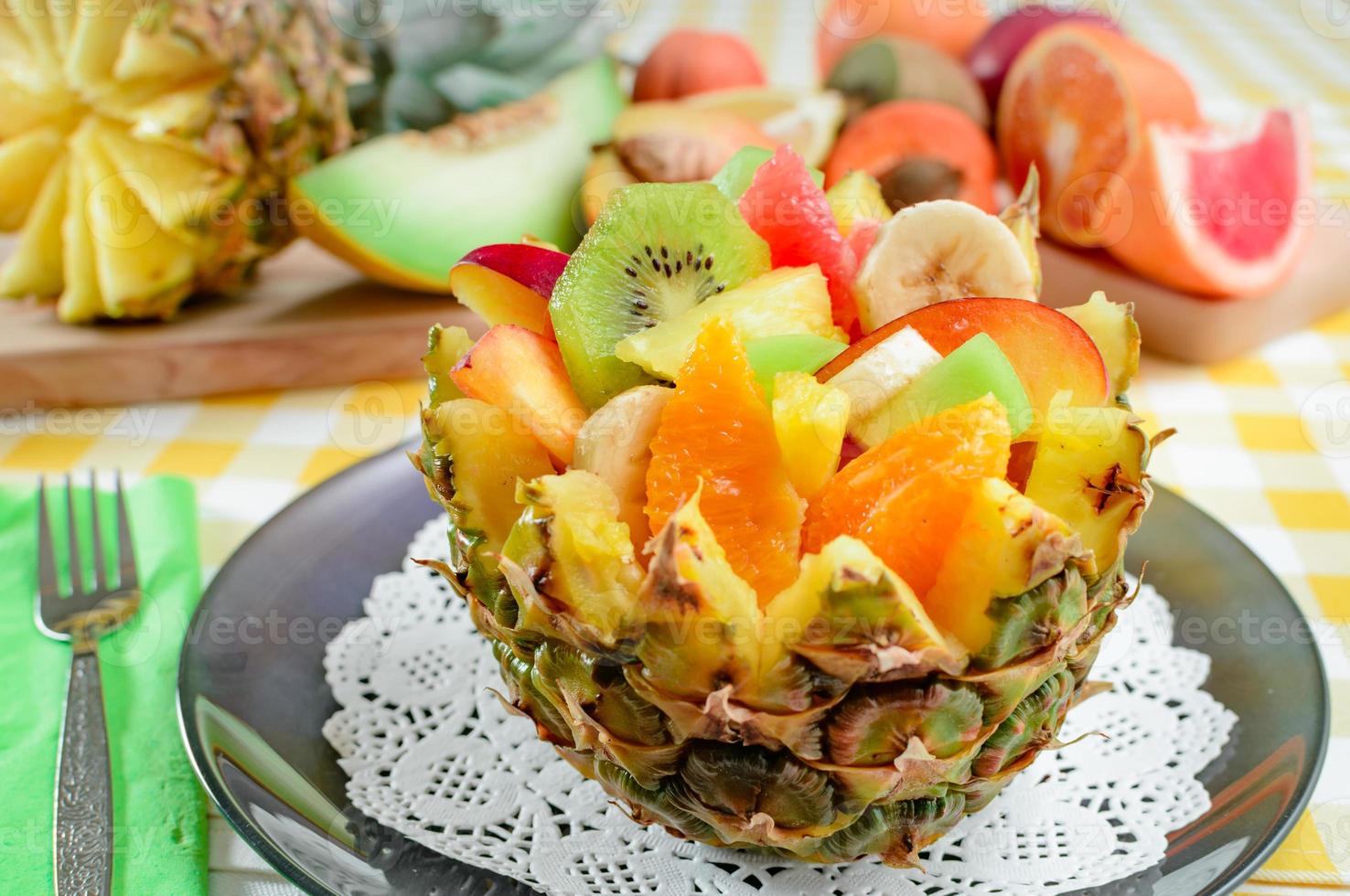 verse fruitsalade met kiwi, banaan, perzik, sinaasappel, rode sinaasappel, abrikoos en meloen in handgemaakte ananaskom. foto