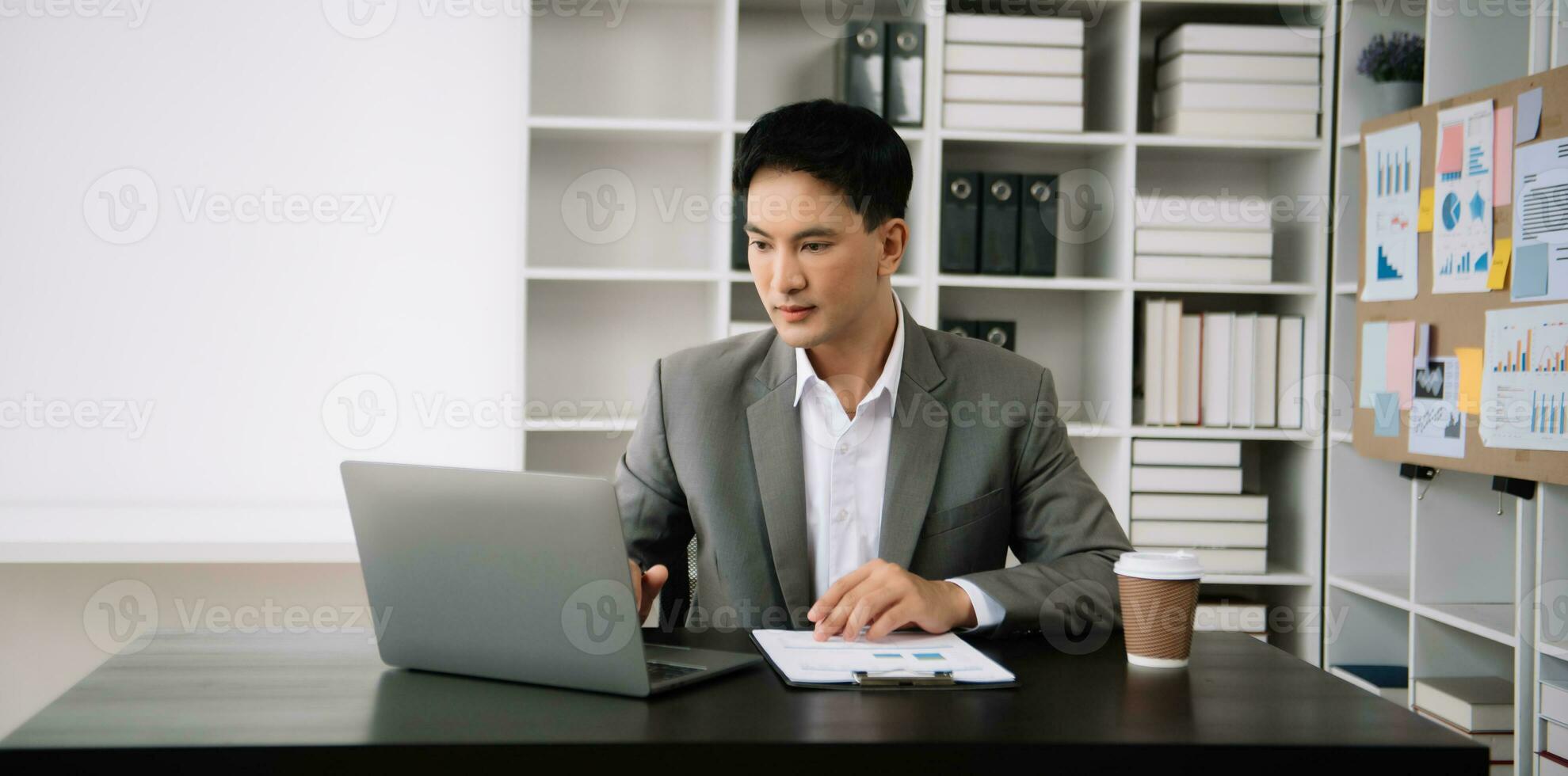 zelfverzekerd Aziatisch Mens met een glimlach staand Holding kladblok en tablet Bij de modern kantoor. foto