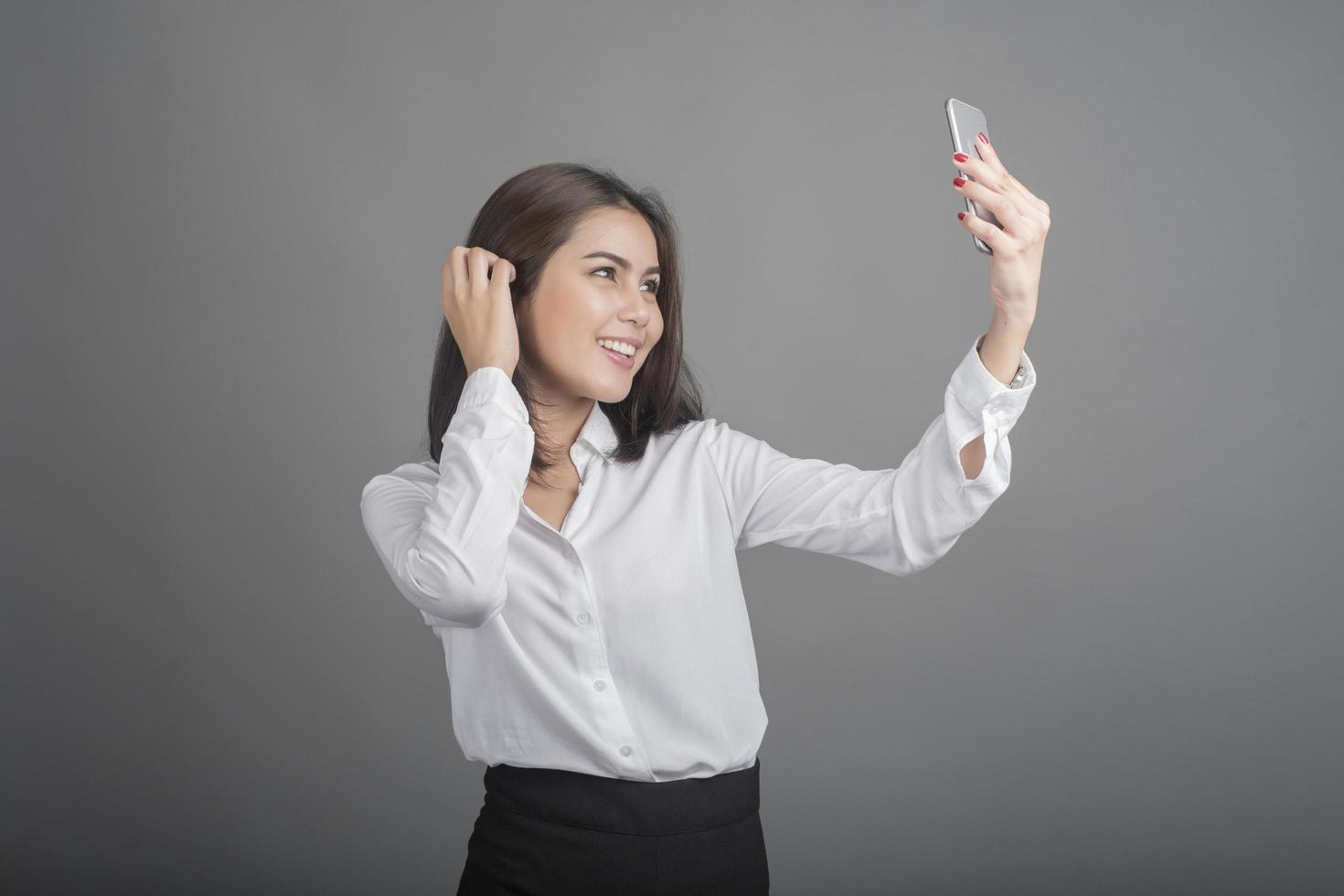 mooie zakenvrouw die smartphone op grijze achtergrond gebruikt foto