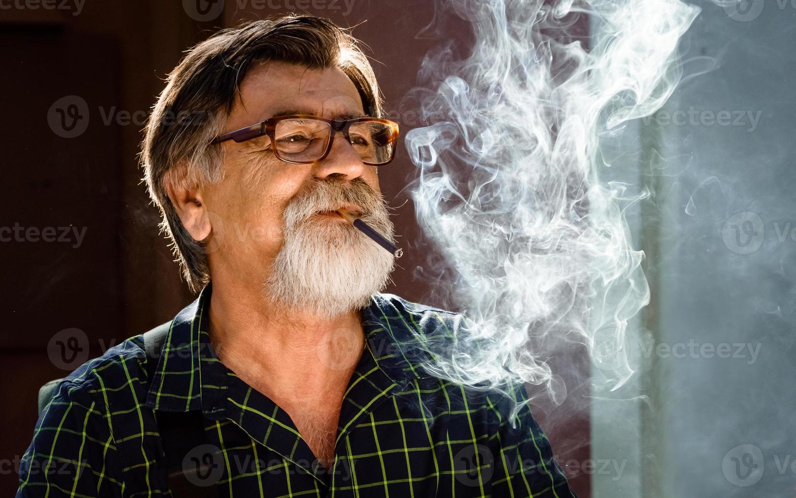 man van middelbare leeftijd met een grijze baard en bril rookt zijn sigaret foto