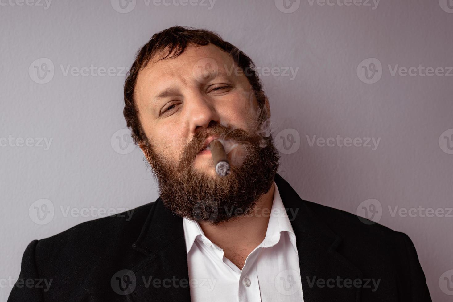 bebaarde man in moderne jas en shirt die zijn sigaar rookt foto