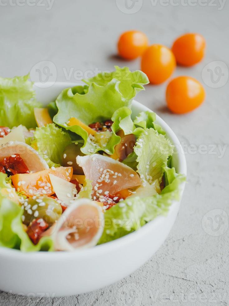 frisse salade van sla, cherrytomaatjes, olijven, zongedroogde tomaten, parmaham, cheddar kaas, parmezaan, olijfolie en sesam. gezond eetconcept. foto