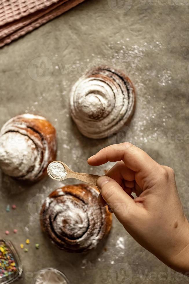 vrouwenhand strooit poedersuiker op vers gebakken kaneelbroodjes foto