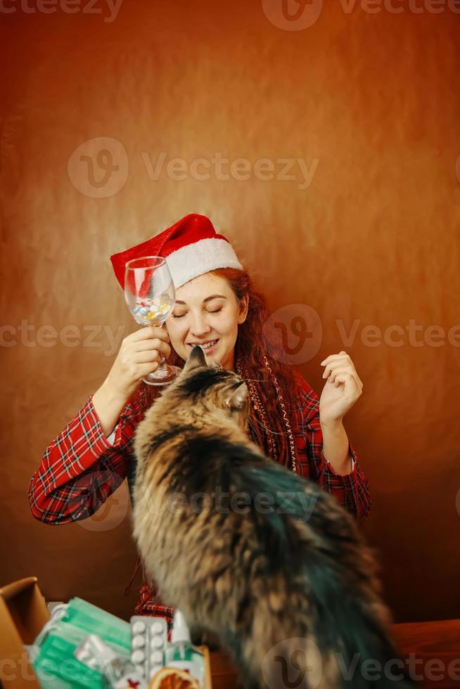 vrouw in kerstmuts houdt glas tabletten vast en speelt met kat. foto