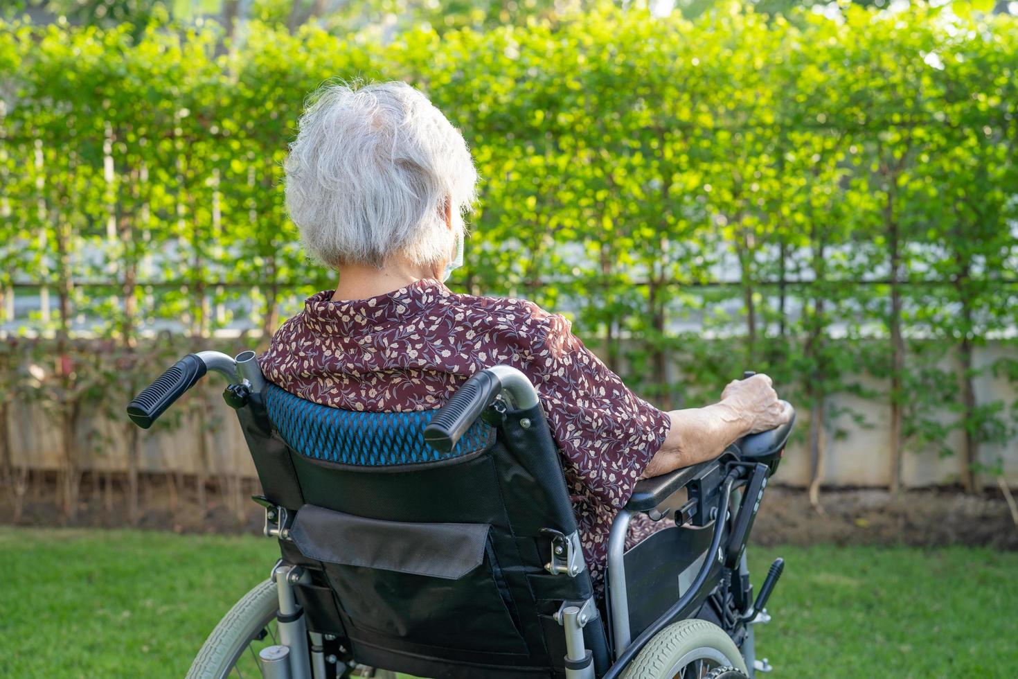 Aziatische senior vrouw patiënt op elektronische rolstoel in park. foto