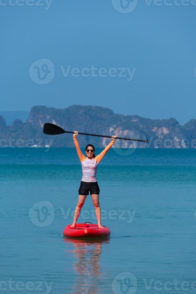 jonge sportieve vrouw die stand-up paddleboard speelt op de blauwe zee op een zonnige dag van de zomervakantie foto