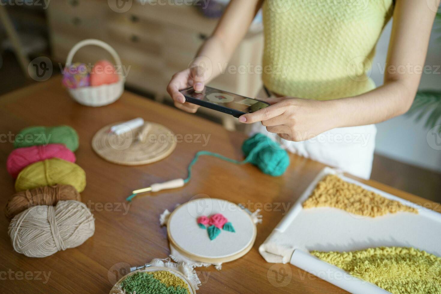 Aziatisch vrouw nemen smartphone foto stempel naald. telefoon posten Aan sociaal netwerken in studio werkplaats. ontwerper werkplaats handgemaakt ambacht project diy borduurwerk