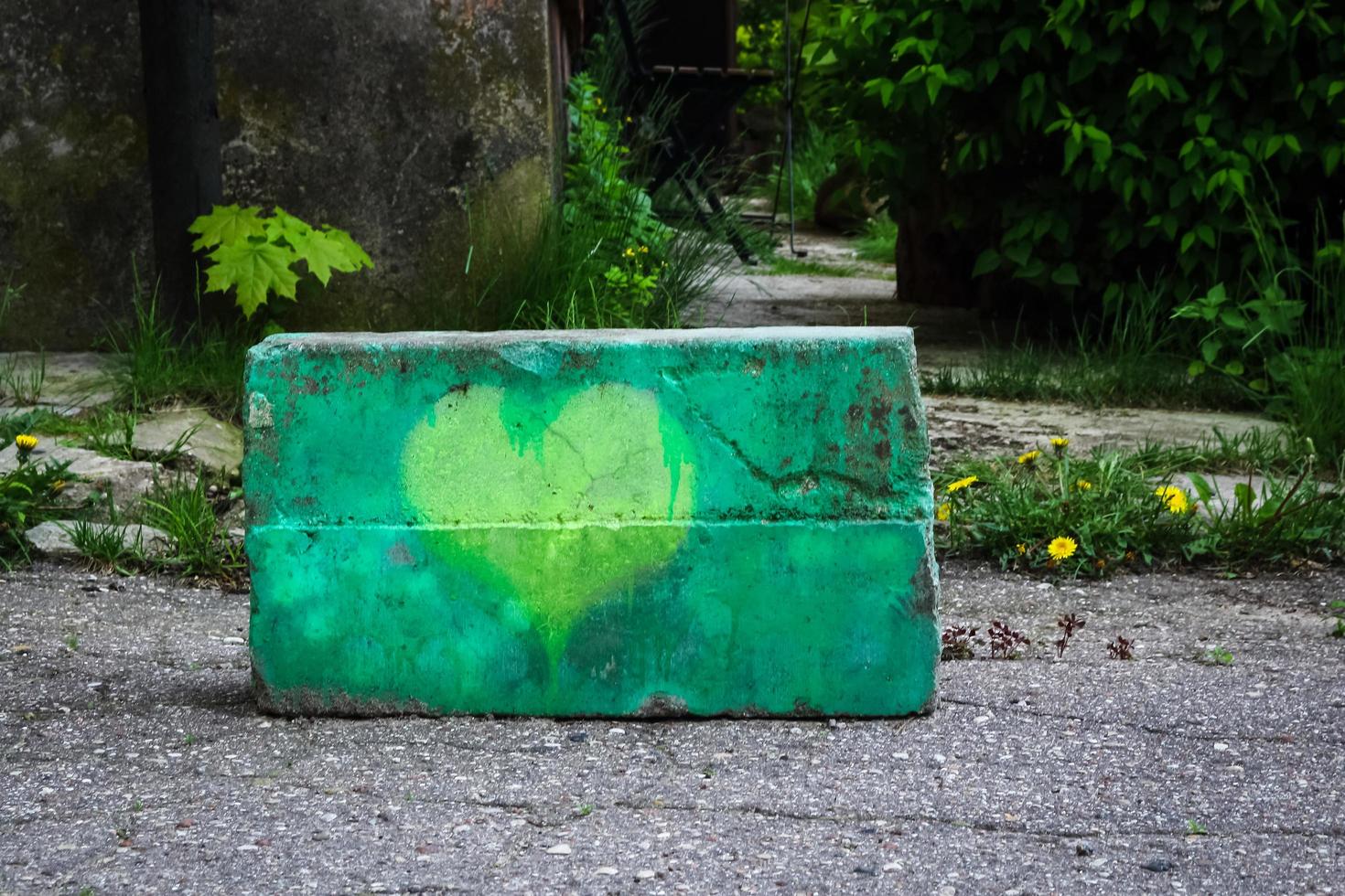 geel geschilderd hart op beton met graspaardebloemen en bomen op achtergrond foto