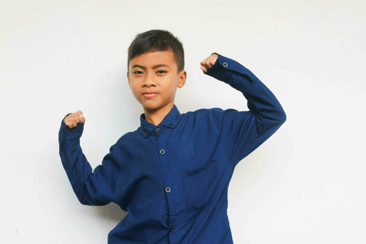 Aziatisch jongen in blauw overhemd demonstreren zijn spieren of biceps Aan de wit achtergrond. toekomst en droom concept foto