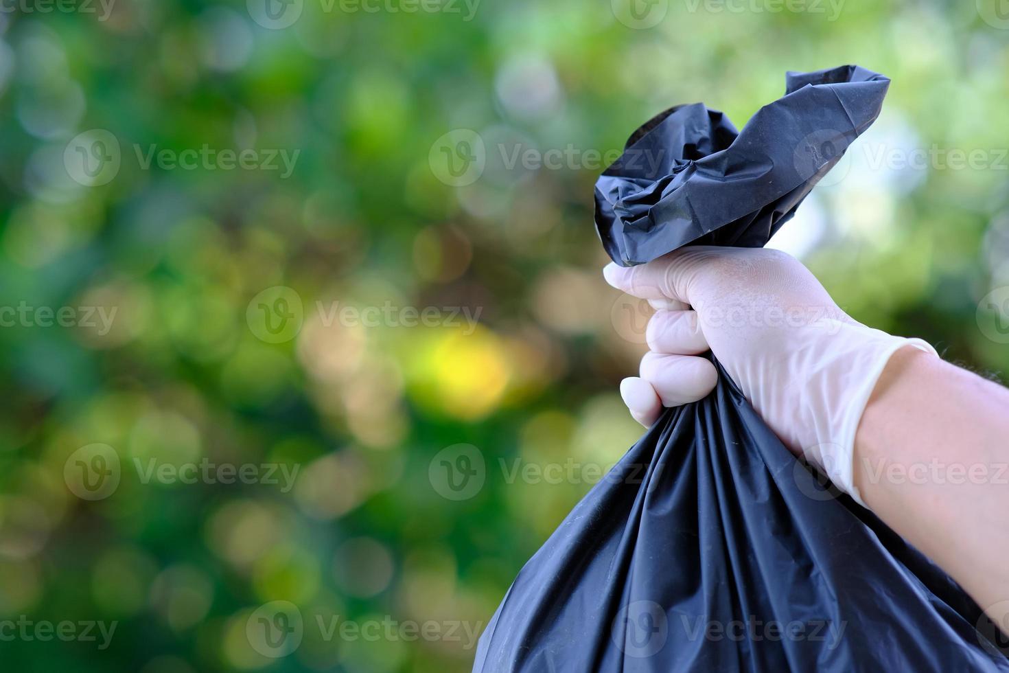 hand met vuilniszak op groene bokehachtergrond en red de wereld en recycle concept foto