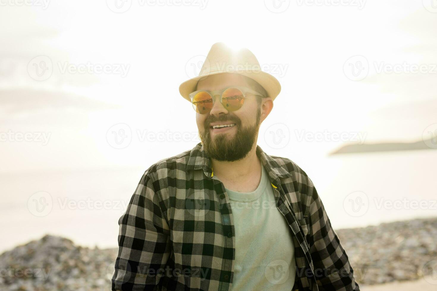 knap en zelfverzekerd. buitenshuis portret van glimlachen Mens vervelend hoed en zonnebril Aan strand. vakantie reizen en zomer toerisme foto