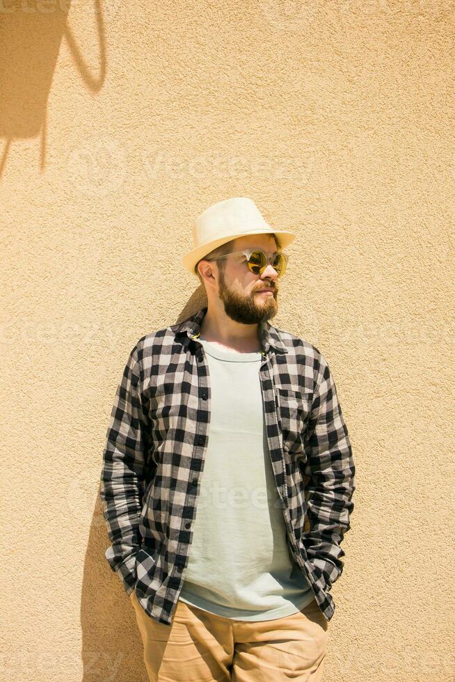 mode millennial elegant Mens poseren Aan straten van Europese stad. gebaard knap hipster Mens poseren in de buurt muur met moeilijk schaduwen Aan heet middag- - zomer vakanties en vakantie concept foto