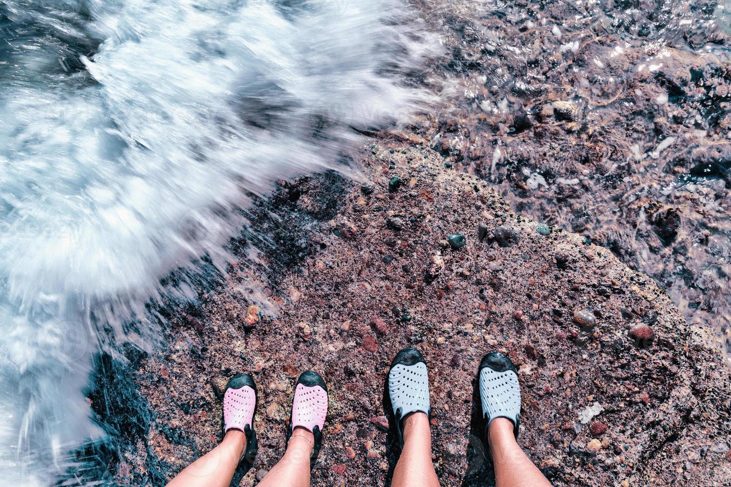 paar staan samen op de stenen oever. voeten van paar vallende watergolf aan de kust. foto