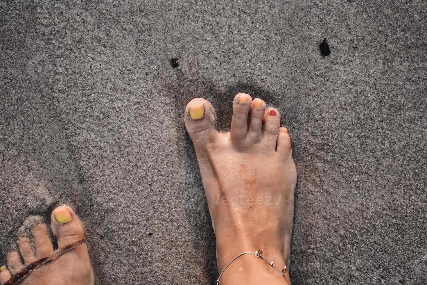 een vrouw met een gekke nagellak die een voetafdruk in het zand probeert te maken. foto