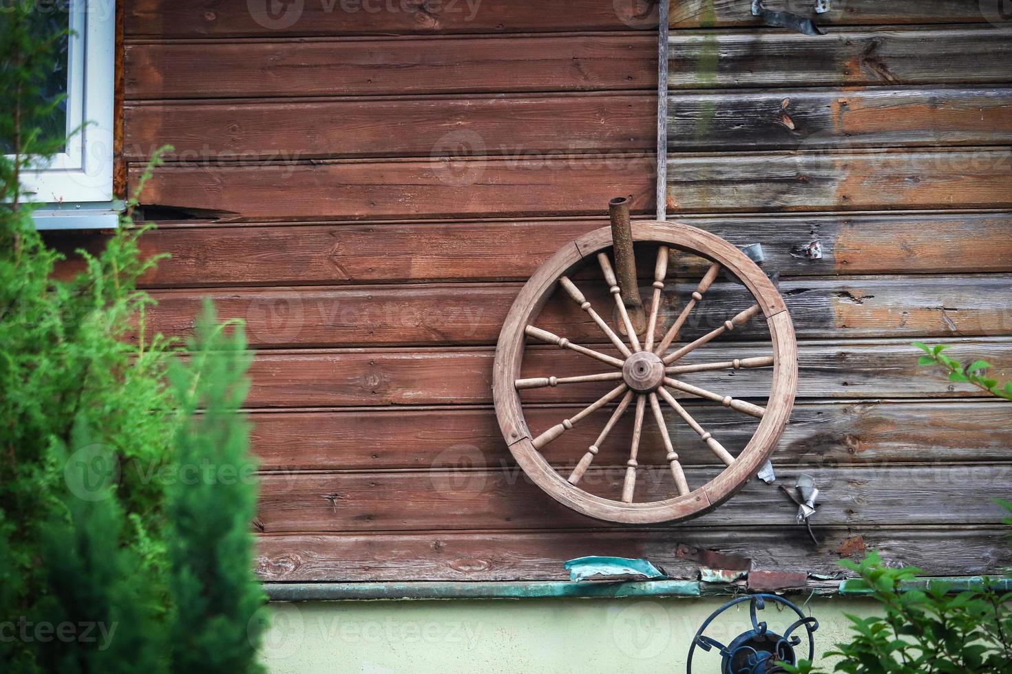 groot oud houten wiel dat aan de houten plankmuur van een landelijk huis hangt foto