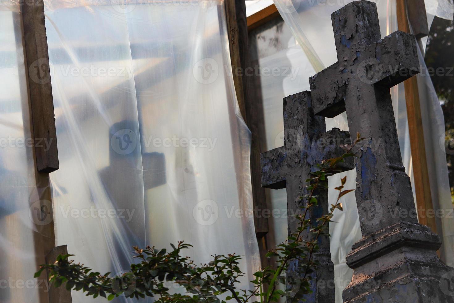 oude begraafplaats in reconstructie met blauw kruis achter een struik en bedekt met plasticfolie op houten steunen foto