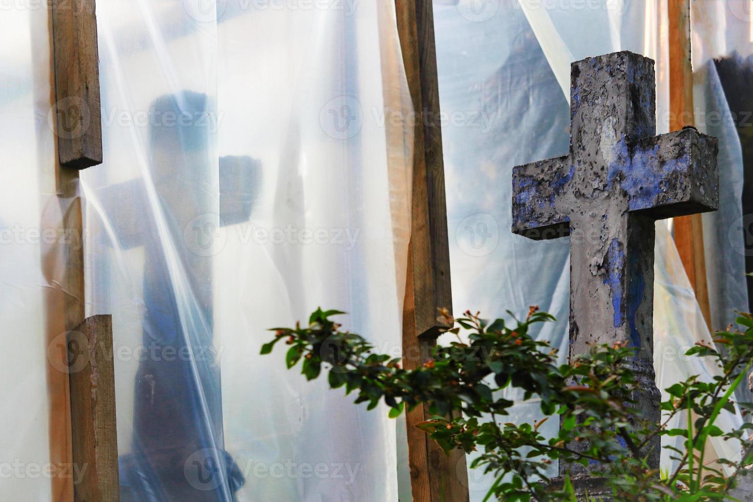 oude begraafplaats in reconstructie met blauw kruis achter een struik en bedekt met plasticfolie op houten steunen foto