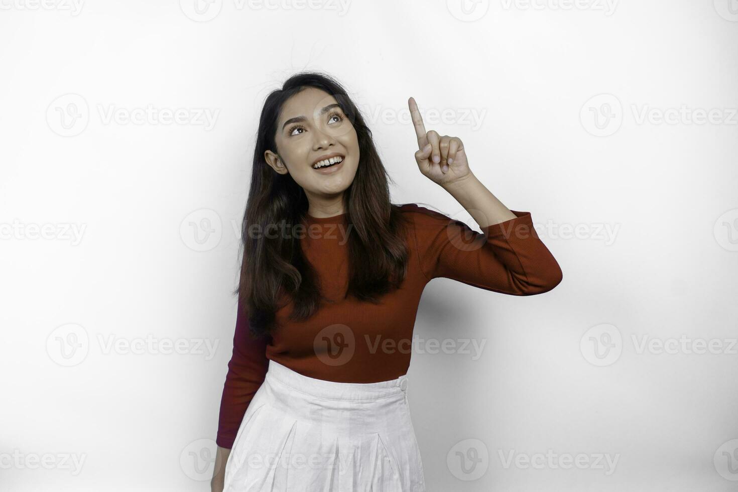 opgewonden Aziatisch vrouw vervelend rood t-shirt, richten Bij de kopiëren ruimte Aan top van haar, geïsoleerd door wit achtergrond foto