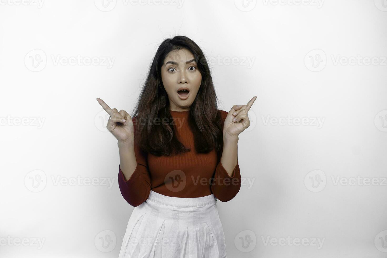 geschokt Aziatisch vrouw vervelend rood t-shirt, richten Bij de kopiëren ruimte Aan naast haar, geïsoleerd door wit achtergrond foto