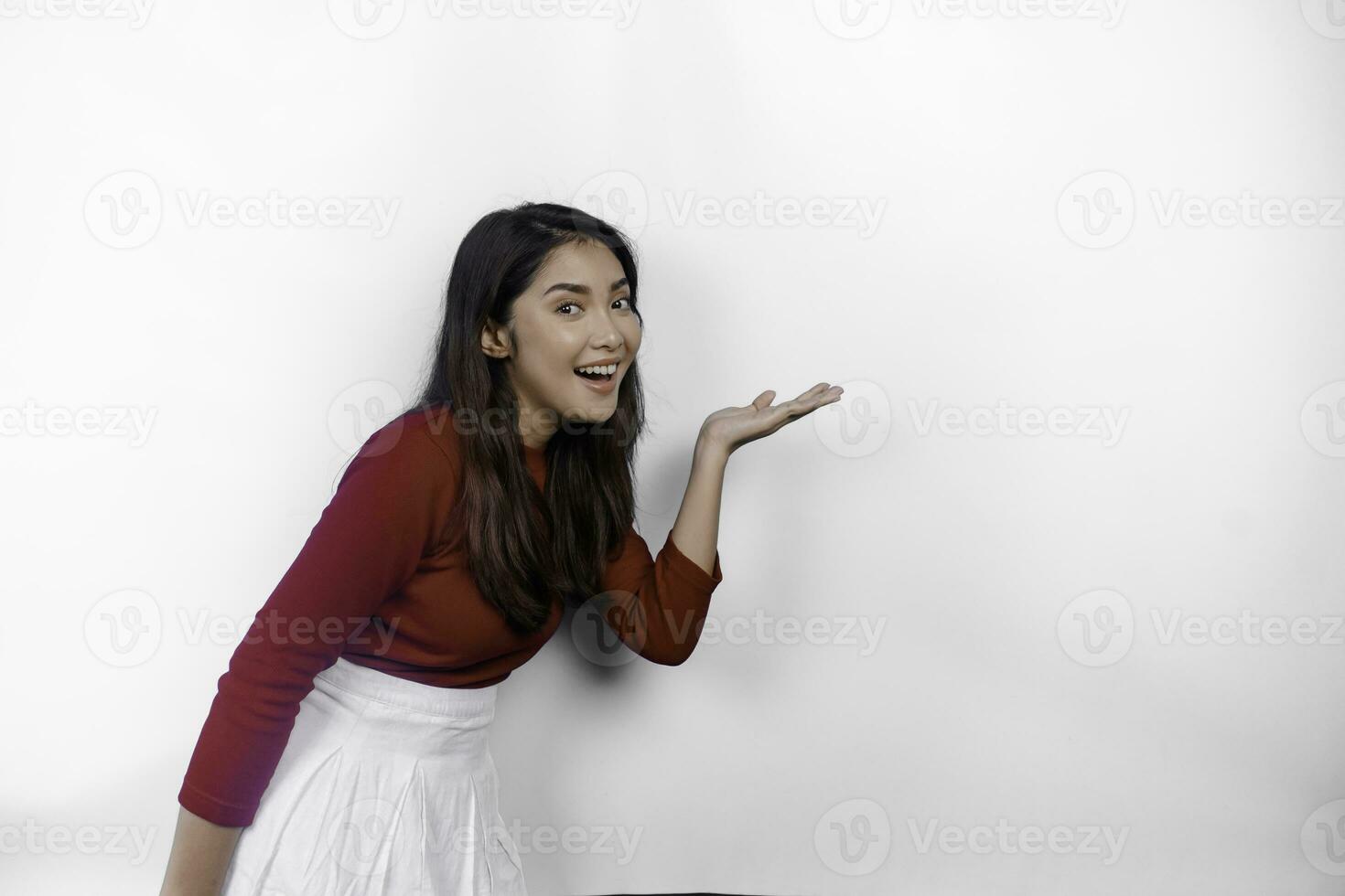 opgewonden Aziatisch vrouw vervelend rood t-shirt, richten Bij de kopiëren ruimte naast haar, geïsoleerd door wit achtergrond foto